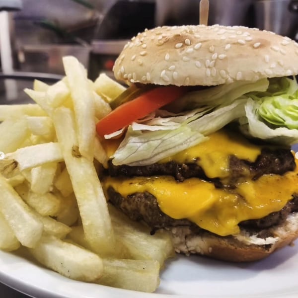 A double cheeseburger with lettuce, tomato, and pickles, served with a side of golden french fries.
