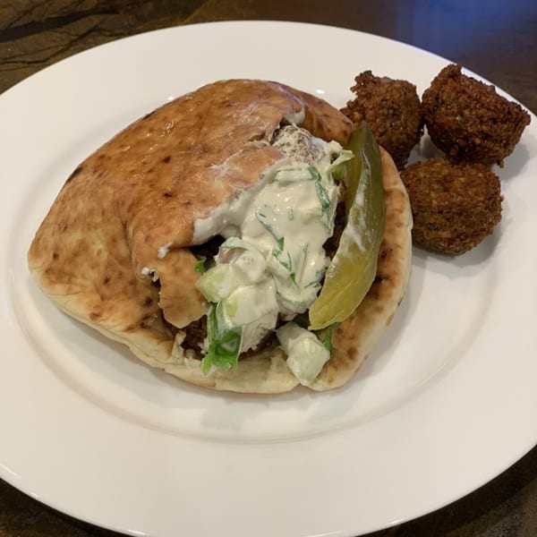 A falafel pita sandwich with tzatziki sauce and a pickle spear, served with three falafel balls.