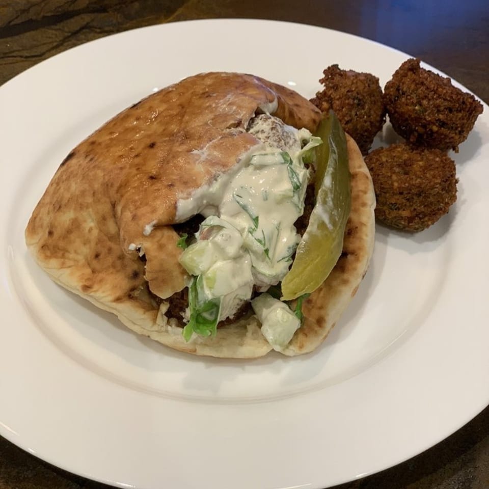 A falafel pita sandwich with tzatziki sauce and a pickle spear, served with three falafel balls.