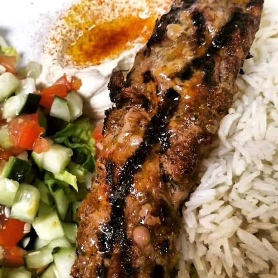 Grilled kabob with rice, hummus, and a fresh salad of diced cucumbers, tomatoes, and lettuce.