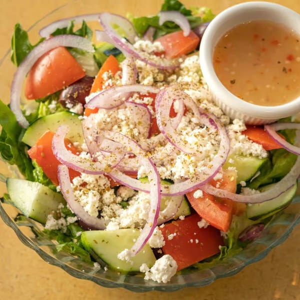 A vibrant Mediterranean salad with lettuce, tomatoes, cucumbers, red onions, feta cheese, and dressing.
