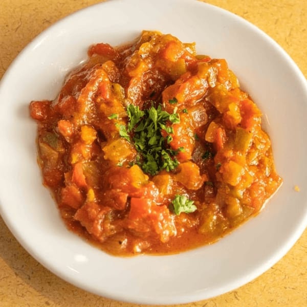 A white plate holds a serving of Mediterranean stew, garnished with fresh parsley.