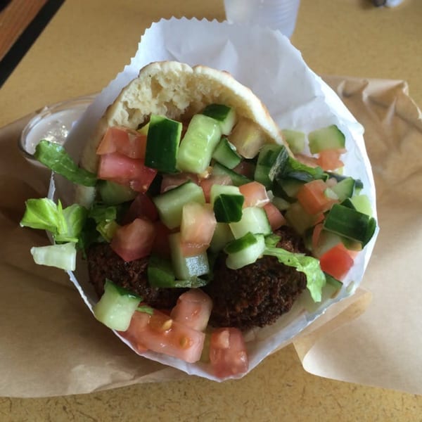 A falafel pita sandwich from Kabab Burger Mediterranean Grill, filled with falafel, diced tomatoes, cucumbers, and lettuce.