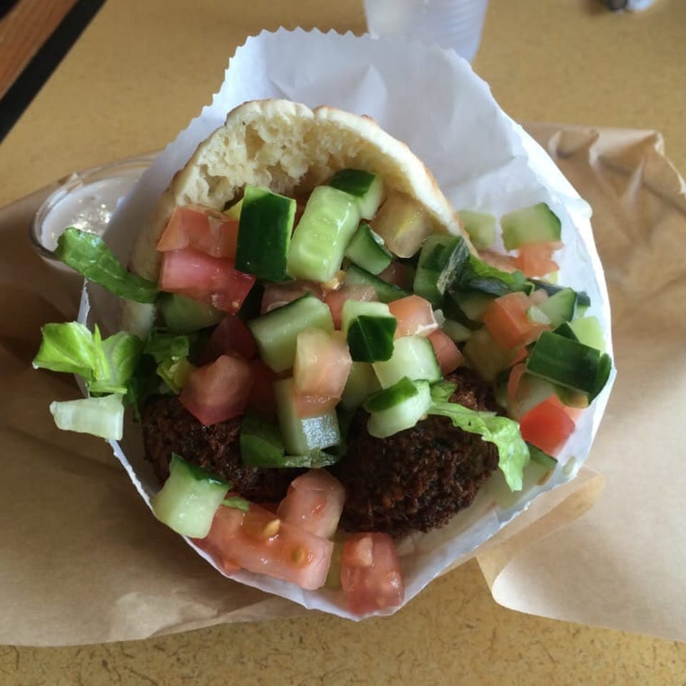 A falafel pita sandwich from Kabab Burger Mediterranean Grill, filled with falafel, diced tomatoes, cucumbers, and lettuce.